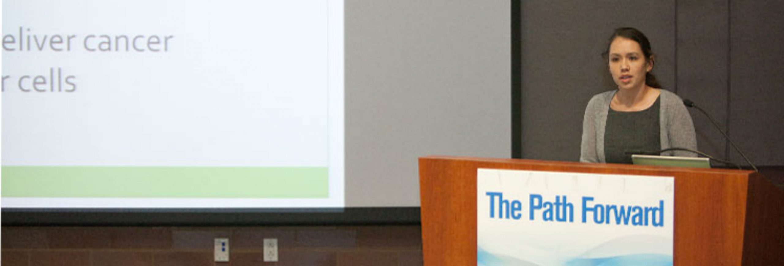 A woman speaks behind a podium with banner "The Path Forward"