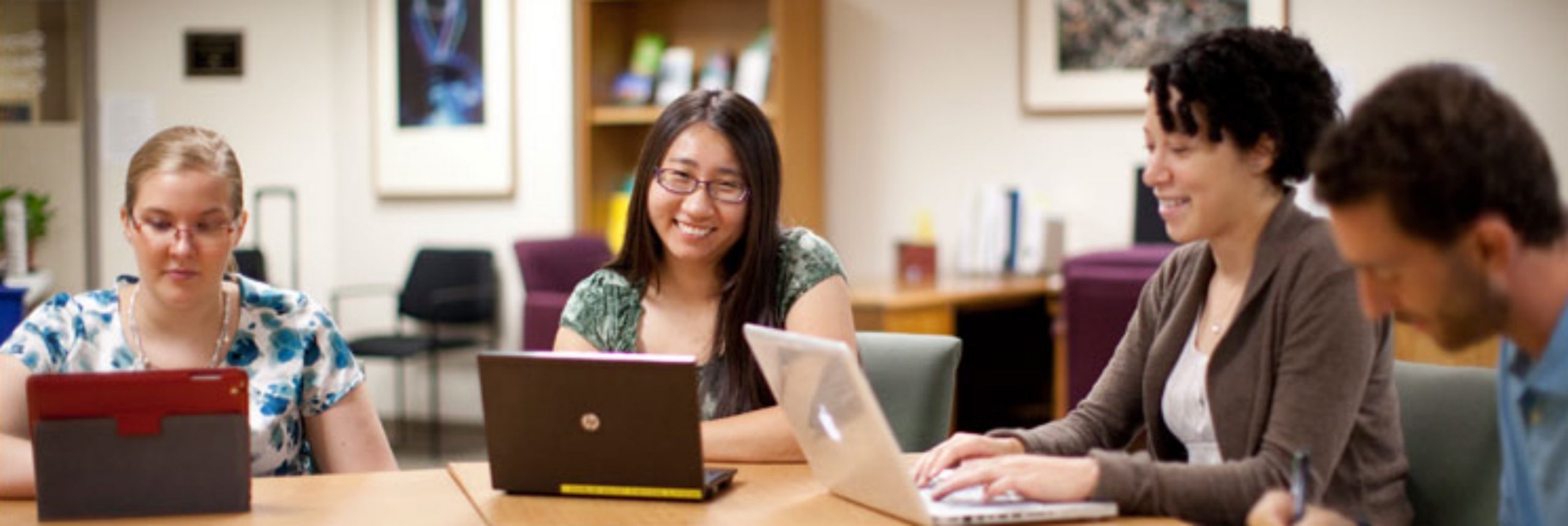 Four people smile at a table while using laptops