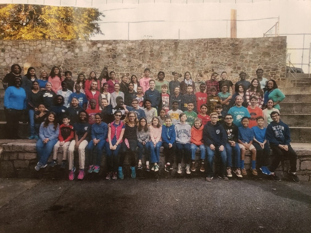 A group of children and adults smiling in front of a stone wall